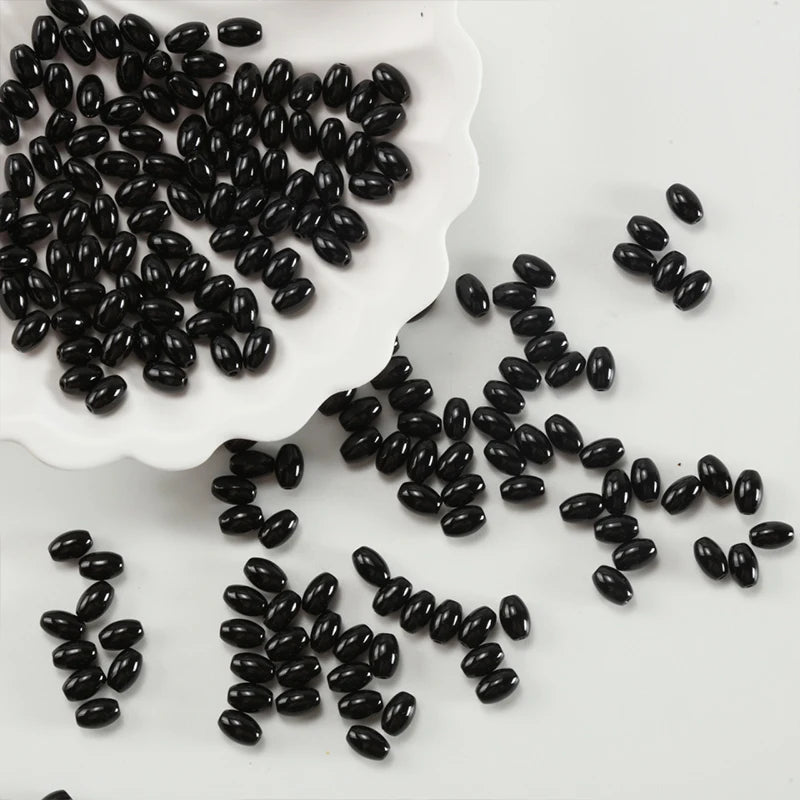 A pile of black oval glass rice grain beads is displayed on a white dish.