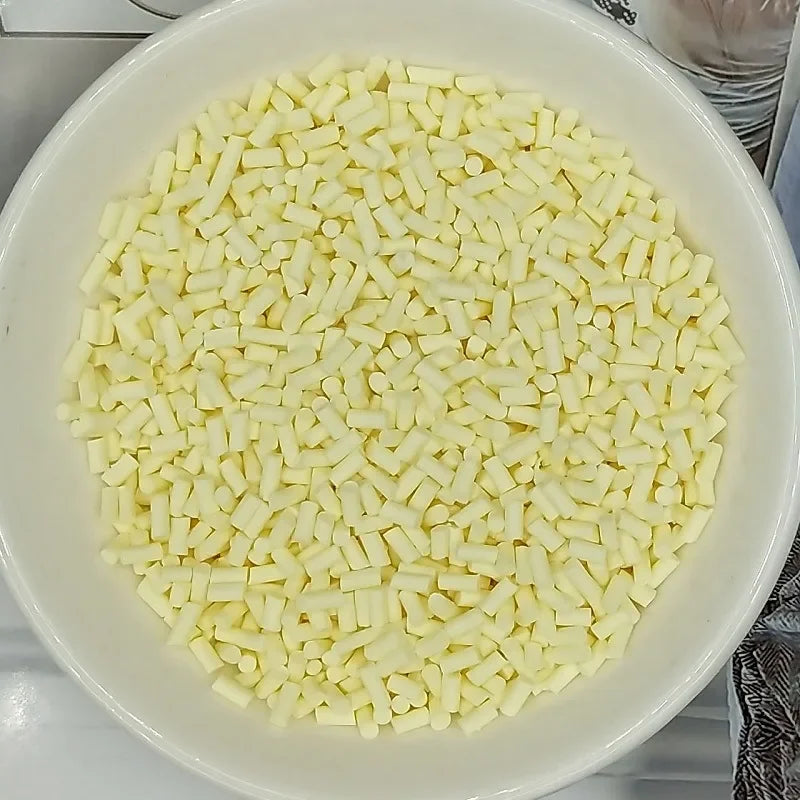 A bowl filled with small, white, rectangular polymer clay slice sprinkles for slime and DIY crafts.