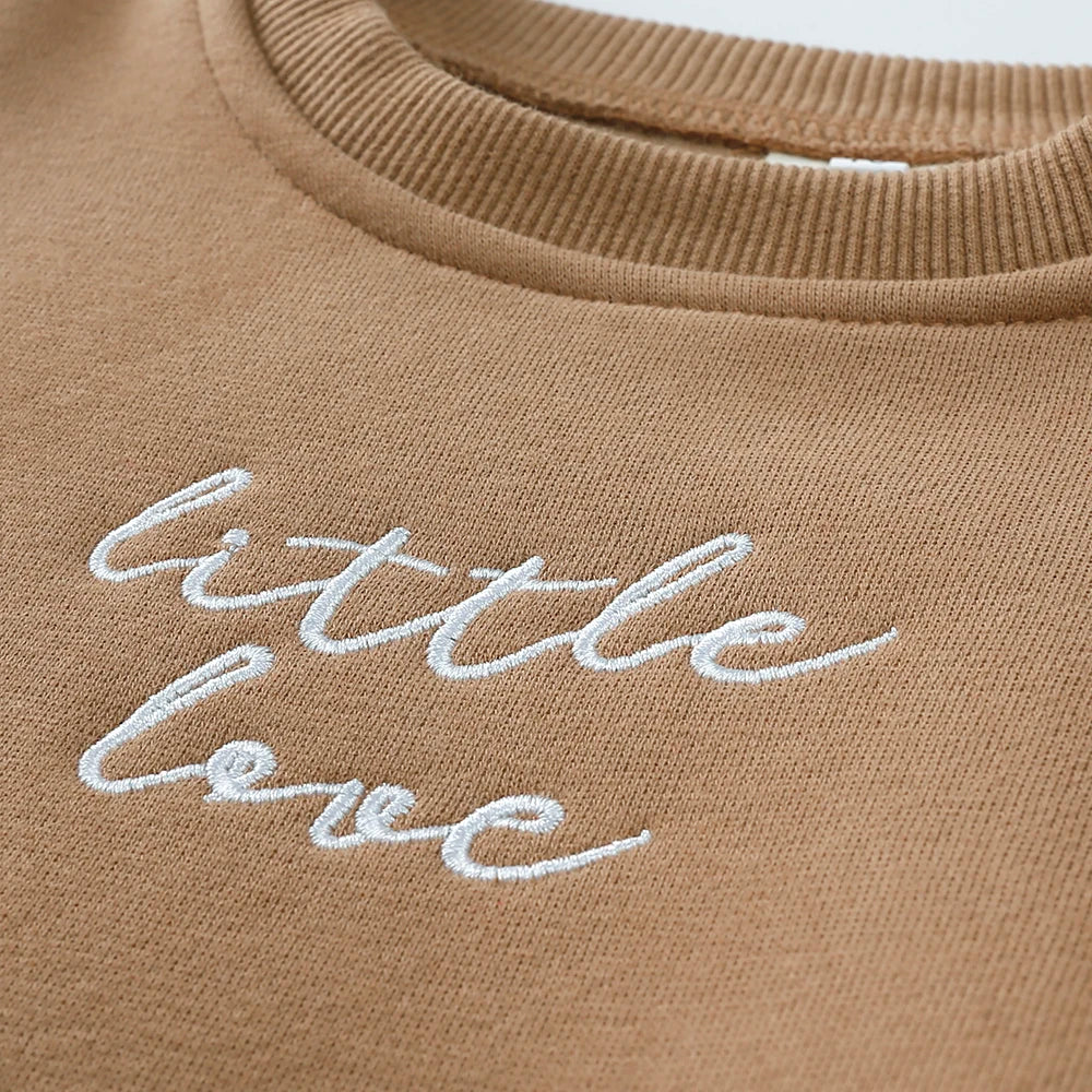 A beige cotton garment featuring white embroidered text that reads little love