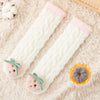 Pair of white coral velvet baby knee-high socks with pink trim and a glowing orange charm on a fluffy background