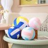 A collection of soft plush volleyball pillows in blue, yellow, and pink resting on a light green table.