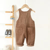 A pair of brown corduroy toddler overalls with heart embroidery hanging on a wooden hanger.