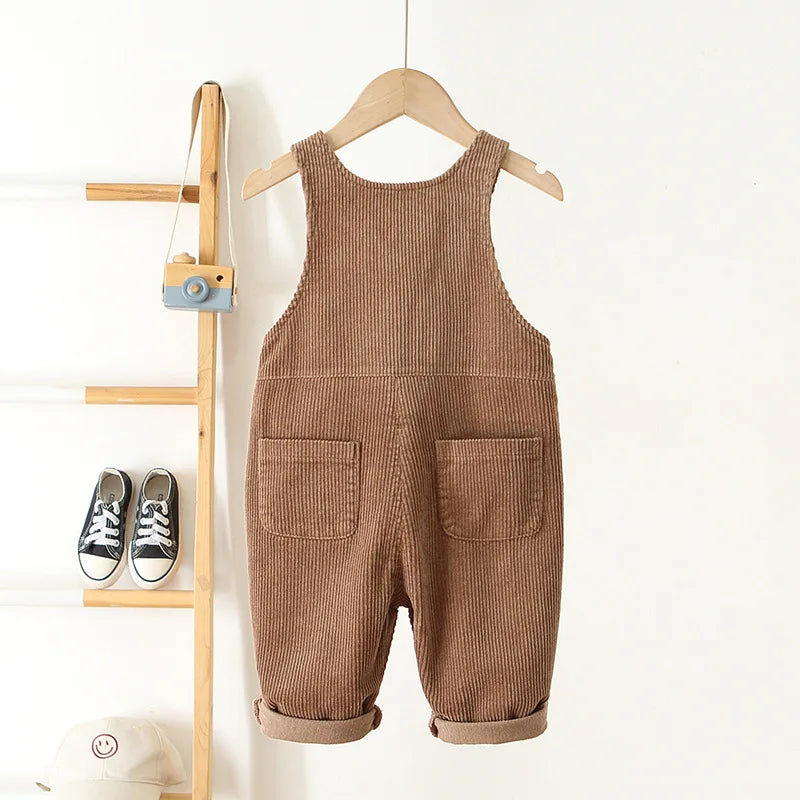 A pair of brown corduroy toddler overalls with heart embroidery hanging on a wooden hanger.