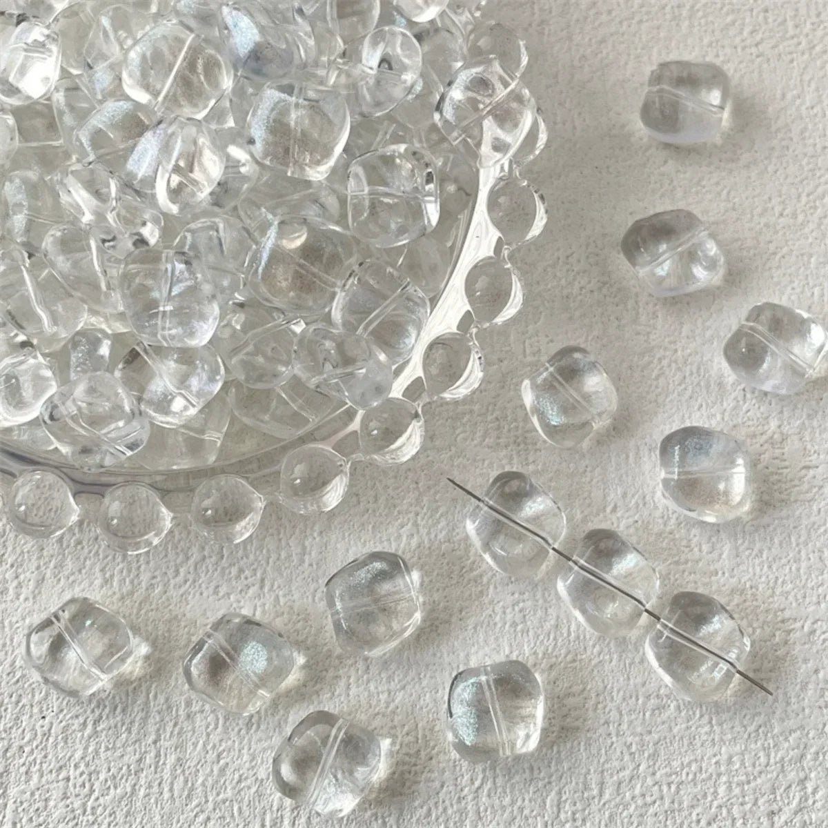 A pile of irregular square geometric glass beads for jewelry making scattered on a white surface.