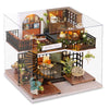 A clear acrylic display of a DIY miniature dollhouse puzzle kit featuring wooden furniture and decorative elements.