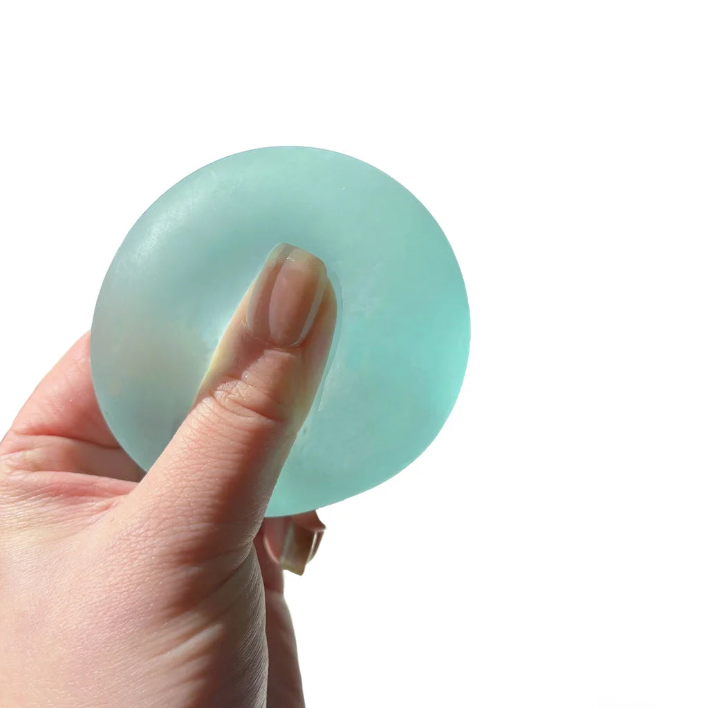A hand is holding a light blue, circular squishy stress relief toy.