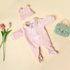 A pink knitted animal romper set for a baby doll, including a matching hat and a small green handbag.