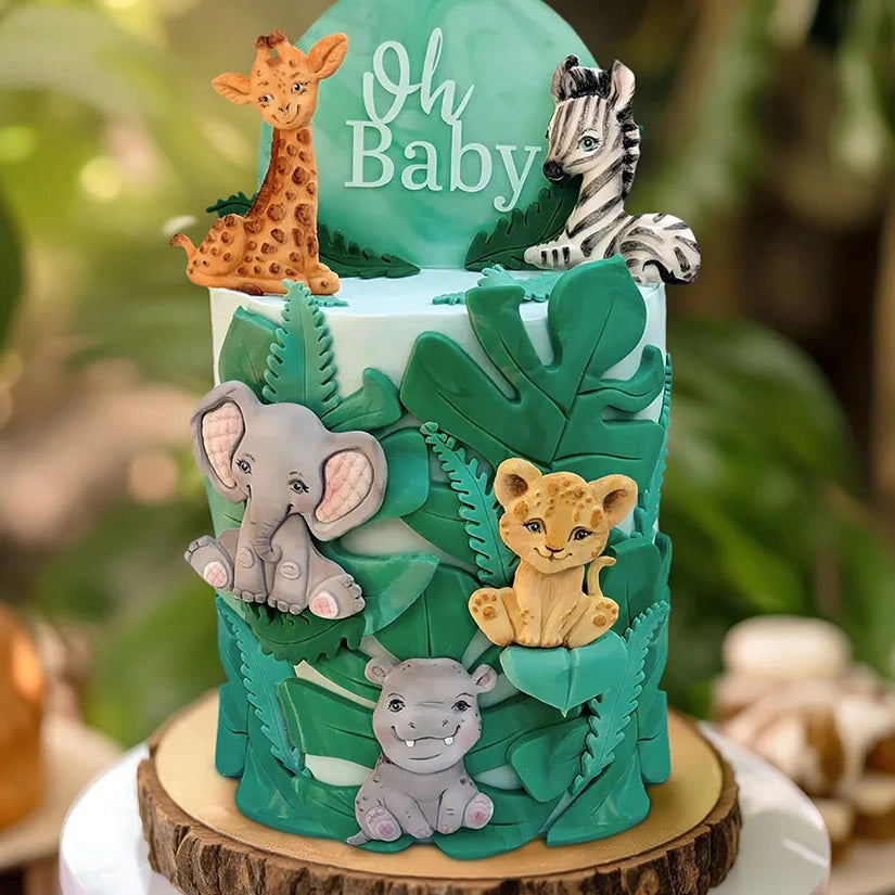 A tiered cake decorated with green foliage and elephant figures for a baby celebration.