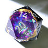 A handmade resin D20 die with a black body and a large purple and blue liquid swirl, featuring silver numbers.