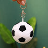 A white soccer ball plush toy hanging from a gold-colored metal ring.