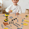 A young boy holds a yellow and black tool set for kids, including drills, screwdrivers, and hammers, on a wooden table.