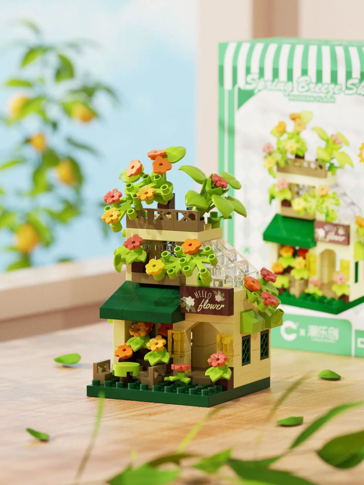A miniature wooden building set featuring a cabin and windmill structure with flowers and greenery.