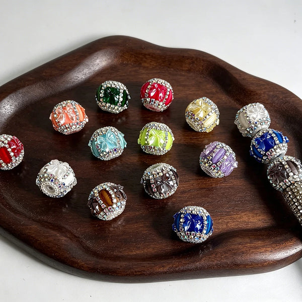 A collection of colorful acrylic bow shape rhinestone beads arranged on a dark wooden platter.