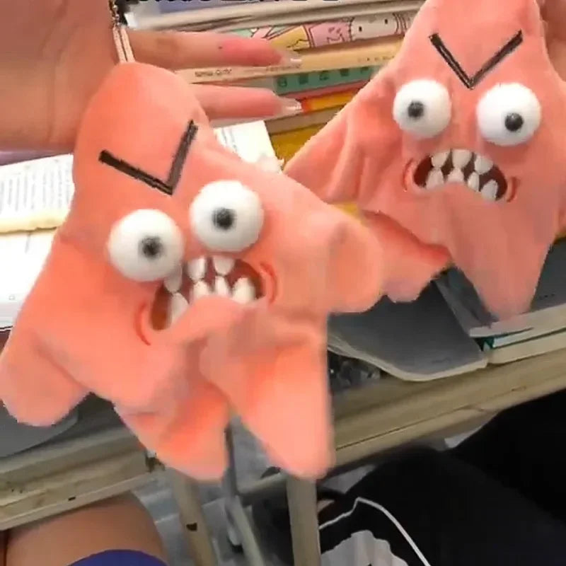 A close-up of an orange plush toy with a fierce expression, held by a hand against a background of books.
