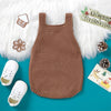 A brown knit baby Christmas romper with white embroidery and a gold-colored holiday design displayed on a teal background.