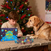 A golden retriever sits next to a wooden table with a blue and yellow dice set for a holiday game.