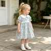 A young girl wearing a light blue floral bubble sleeve dress and white socks standing outdoors.