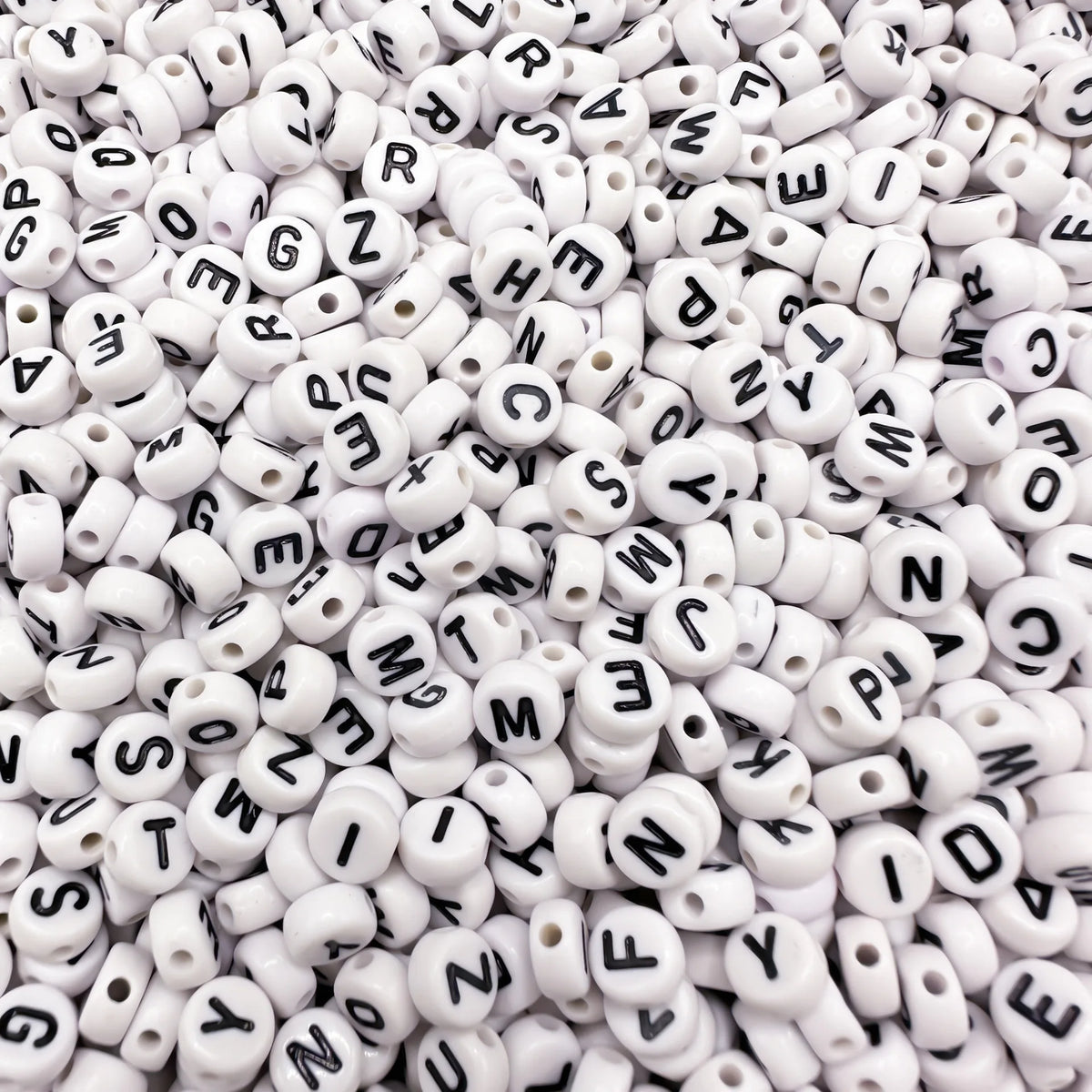A close-up view of small white acrylic alphabet letter beads scattered in a pile.