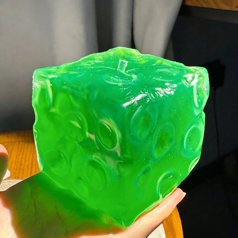 A hand holds a translucent green squishy stress ball made of coconut oil for relaxation.