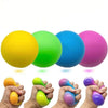 A hand holds a bright yellow slow rising squishy stress ball next to various colored squishies.