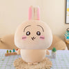 A soft pink Chiikawa plush doll resembling a rabbit, sitting on a woven mat.