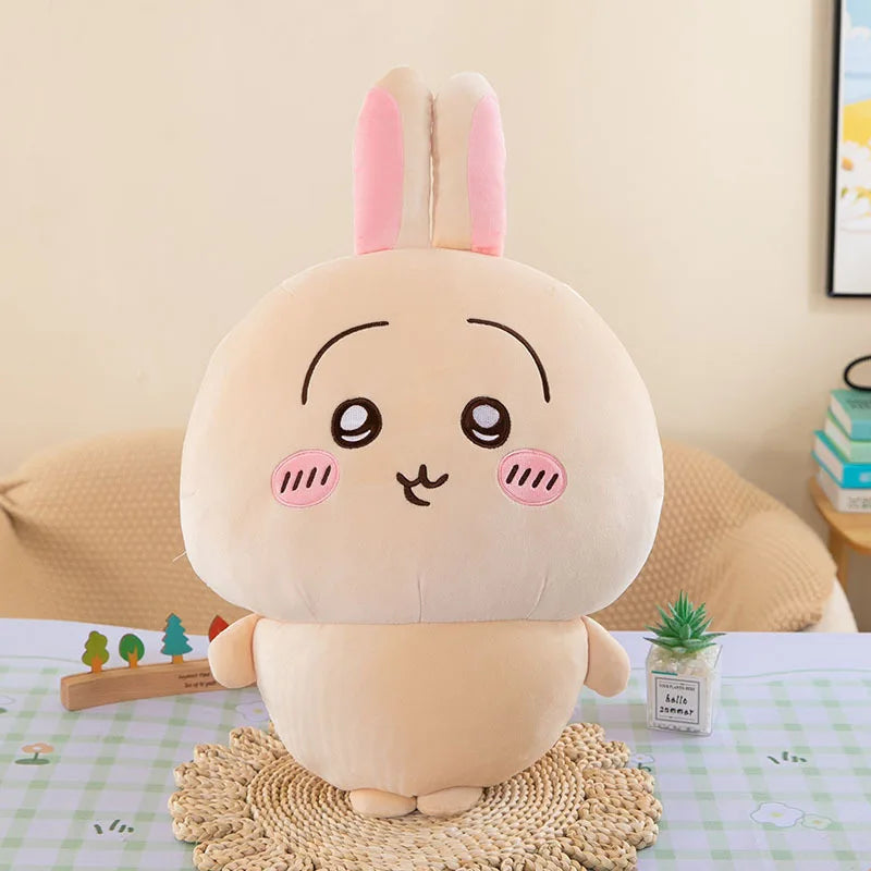A soft pink Chiikawa plush doll resembling a rabbit, sitting on a woven mat.
