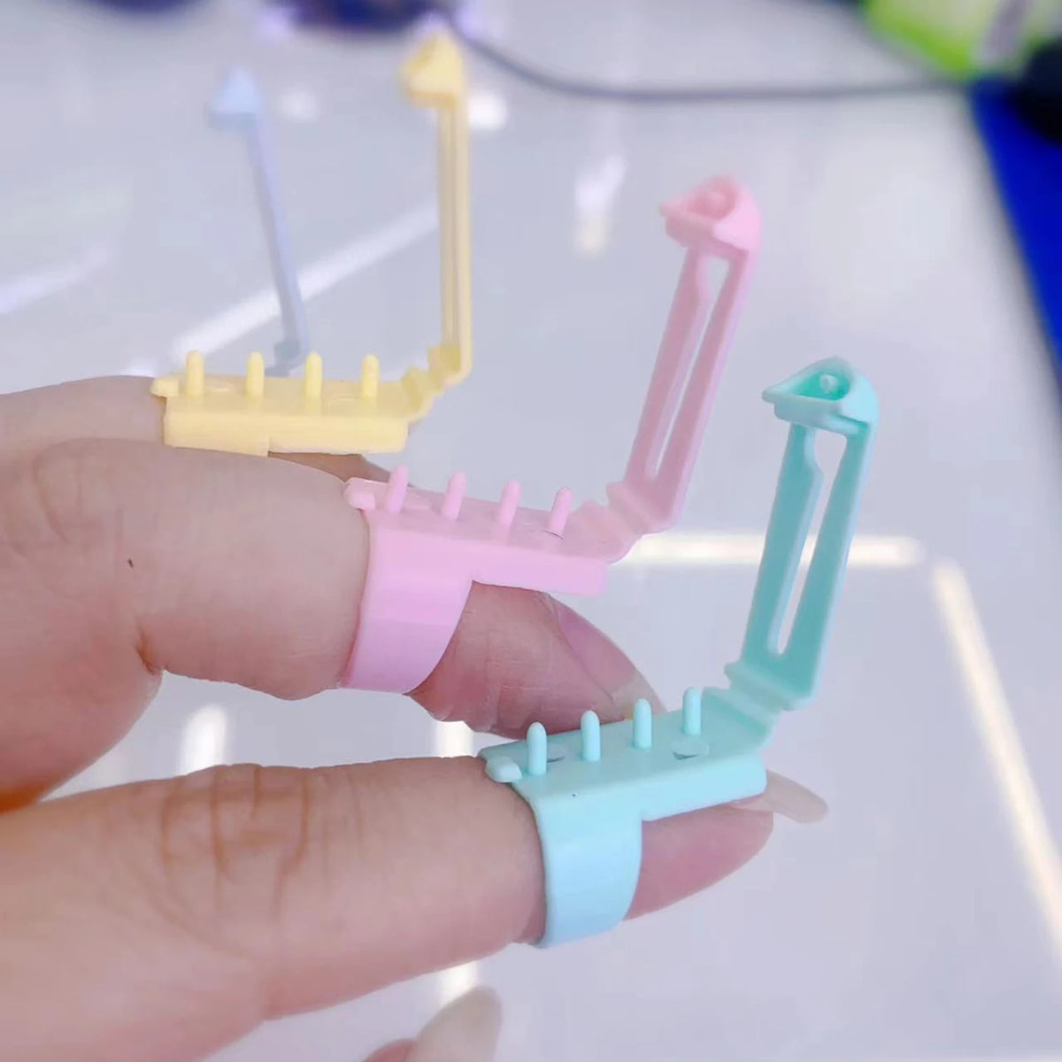 A hand holds three colored ergonomic yarn guide rings for crochet and knitting.