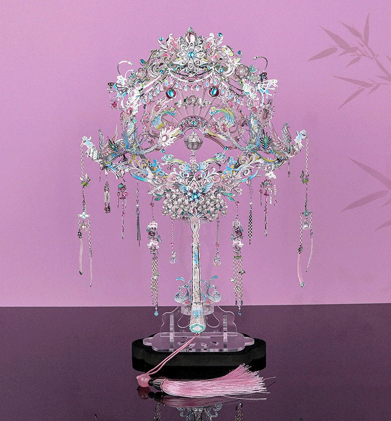 A detailed DIY 3D metal puzzle model kit shaped like a phoenix coronet, displayed on a stand against a pink background.