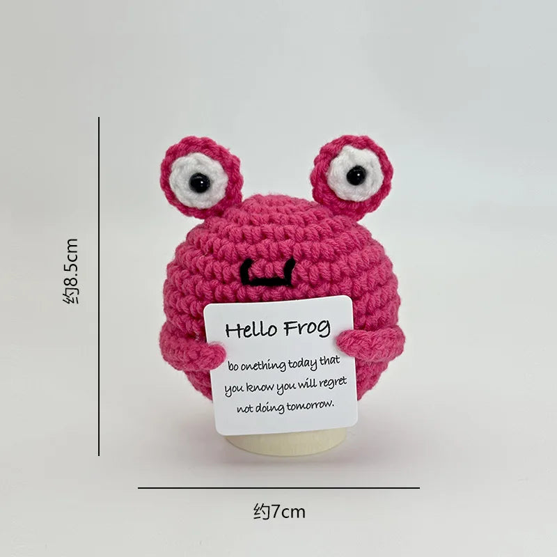 A pink crocheted frog ornament with large eyes and a black mouth, displayed against a white background.