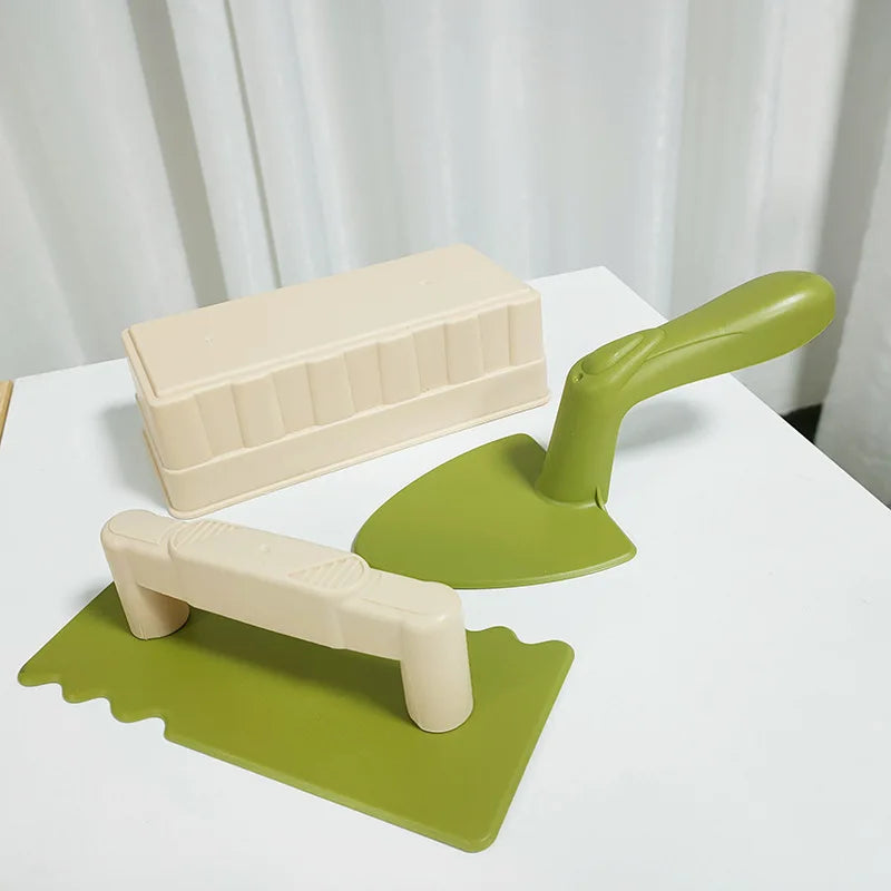 A beige sand and snow building play set featuring a shovel and brick molds on a white surface.