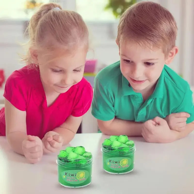 Two children are looking at jars of green slime putty toys on a white table.