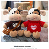 A plush cow doll wearing a red sweater with a heart design, sitting on a surface.