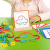A child's hand holds a wooden stick and ring puzzle on a green table with various colored wooden rings and sticks.