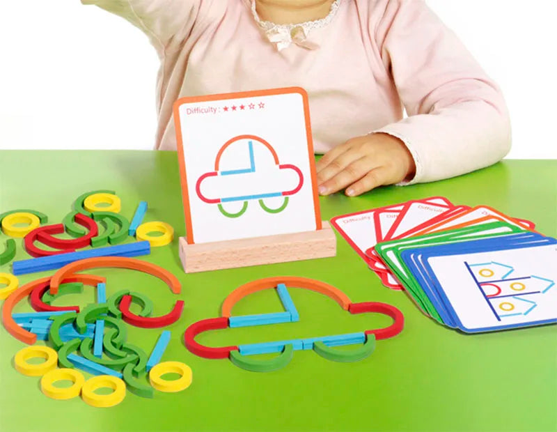 A child's hand holds a wooden stick and ring puzzle on a green table with various colored wooden rings and sticks.
