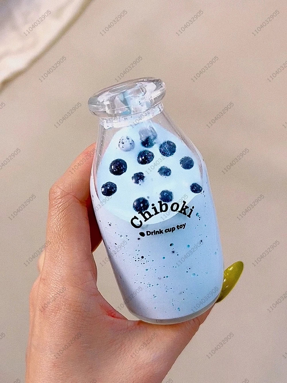 A hand holds a clear glass bottle filled with blue liquid and dark blue spherical toys labeled Chiboki