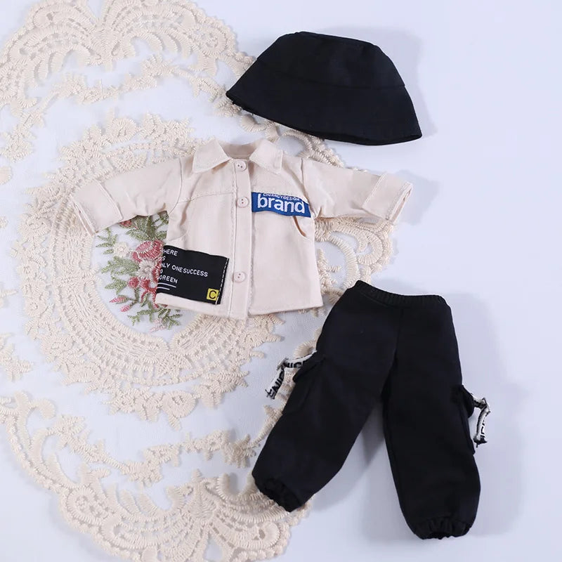 A set of beige and black clothing for a doll including a dress, pants, and a hat.
