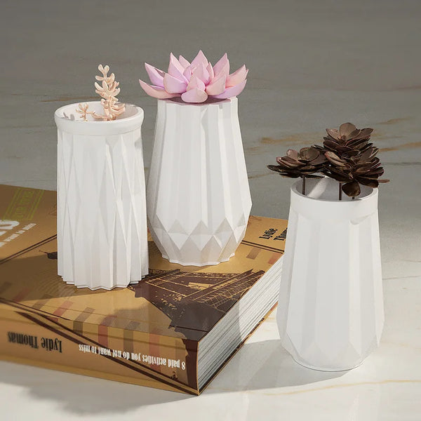White ceramic flower pots with pink and brown floral designs displayed on a book.
