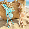 Beaded keychain set featuring starfish and seashell charms hanging from a woven straw bag on the sand.