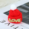 A bright red knitted hat with a white pom-pom and the word LOVE embroidered in gold thread.