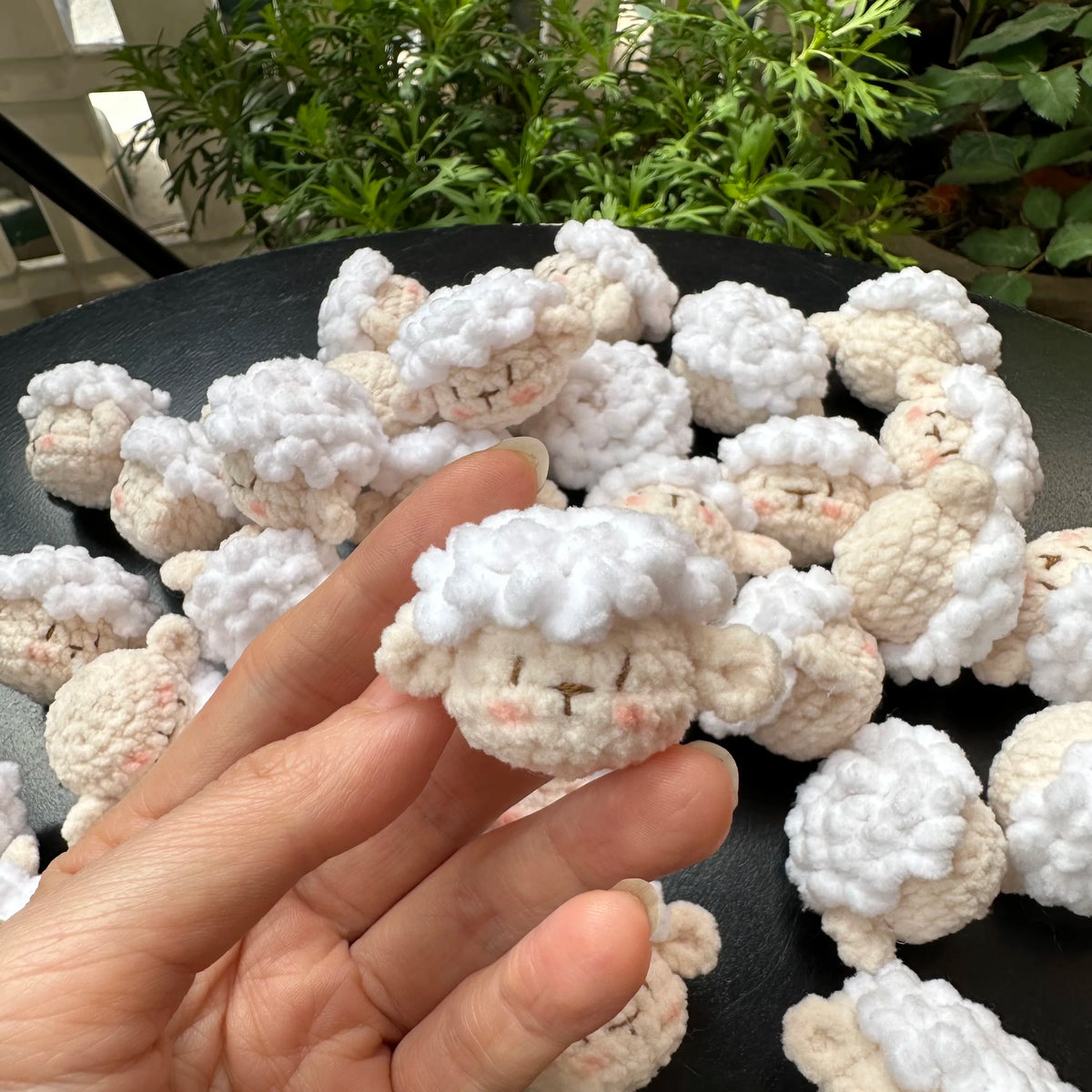 A hand holds a small white crocheted animal keychain, resembling a rabbit or chick.