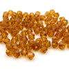 A pile of faceted bicone crystal glass beads in a golden amber color for jewelry making