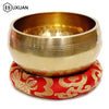 A brass singing bowl resting on a red fabric cushion with gold embroidery.