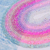 A close-up of iridescent pink and blue faceted crystal rondelle beads arranged in a spiral pattern.