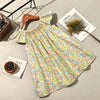 A light green floral smocked summer dress with flying sleeves laid out on a neutral surface.