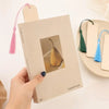 A hand holds a blank wooden bookmark with a photo insert and a pink tassel on a light background.