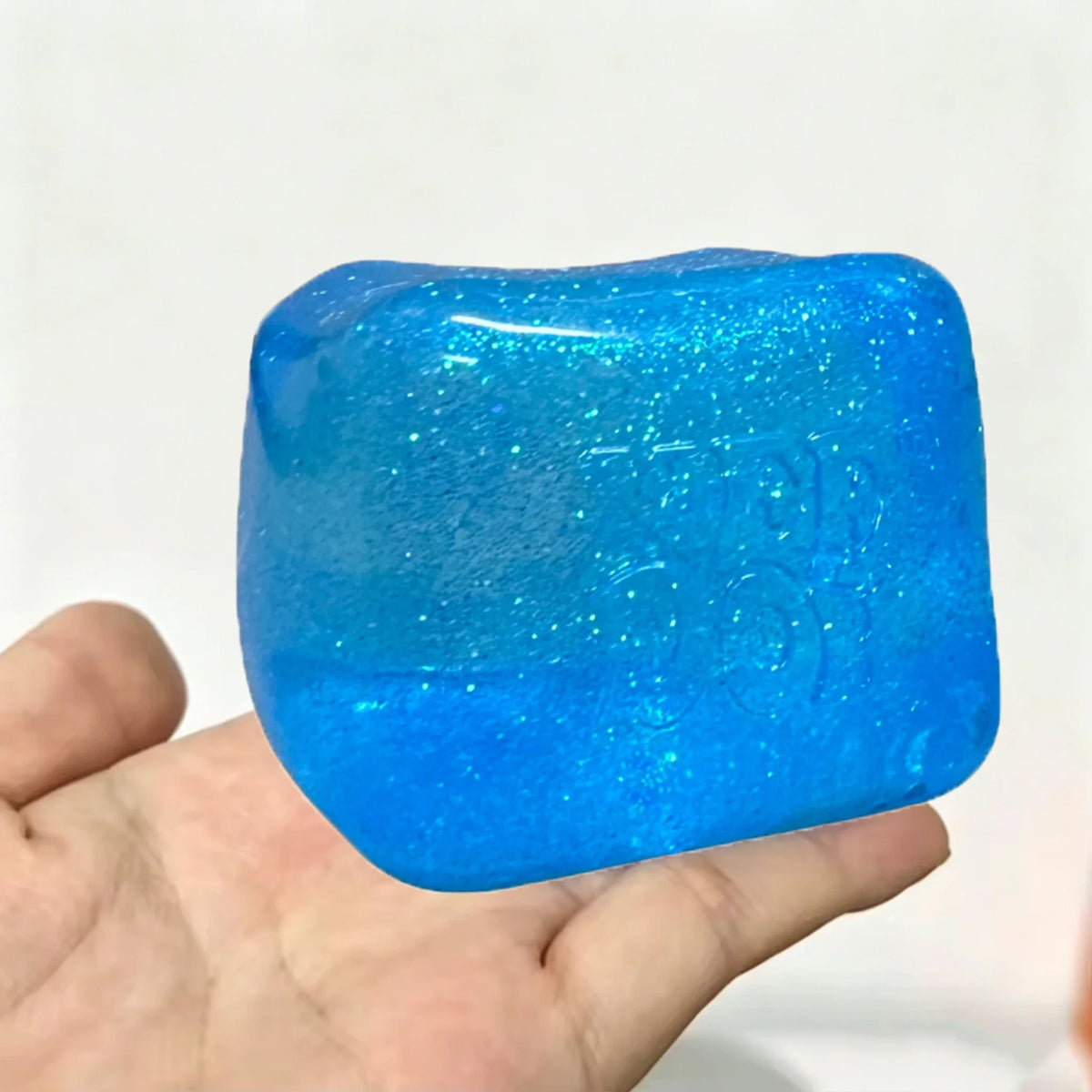 A hand holds a bright blue glitter ice cube sensory fidget toy.