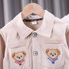 A light beige corduroy jacket for a child, featuring embroidered bear designs on the pockets.