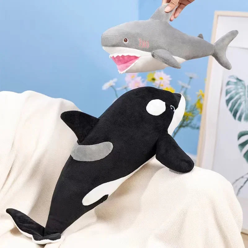 A black and white killer whale plush toy is shown next to a gray great white shark plush toy.