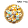 A pile of ten colorful, round silicone beads in various shades of orange, yellow, and green on a wooden plate.