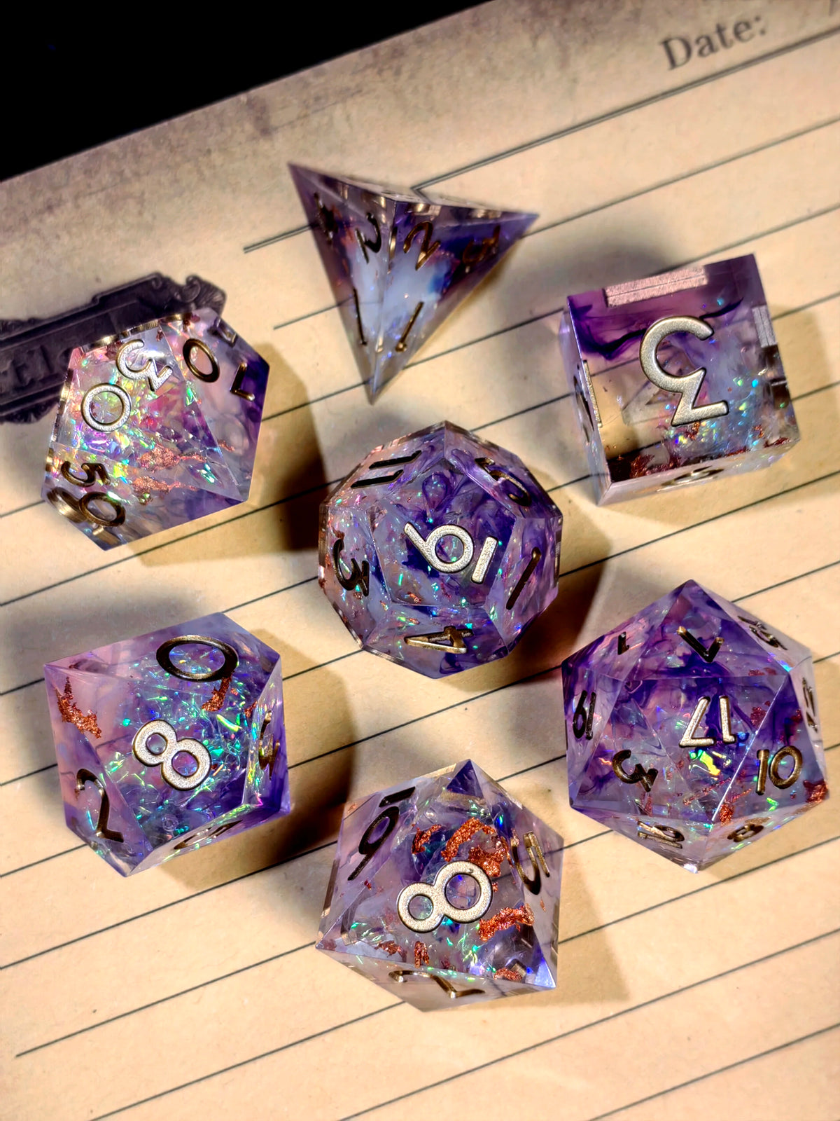A collection of handcrafted resin polyhedral dice in light purple with gold numbers scattered on lined paper.